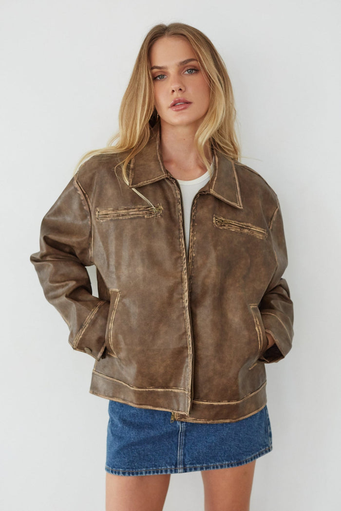 Woman wearing a brown leather jacket and blue denim skirt against a white background