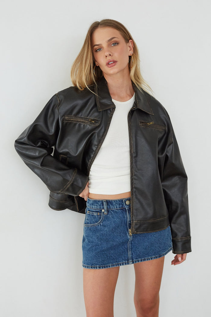 Woman wearing a black leather jacket and blue denim skirt against a white background