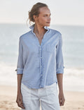 Woman wearing a light blue shirt and white pants on a beach.