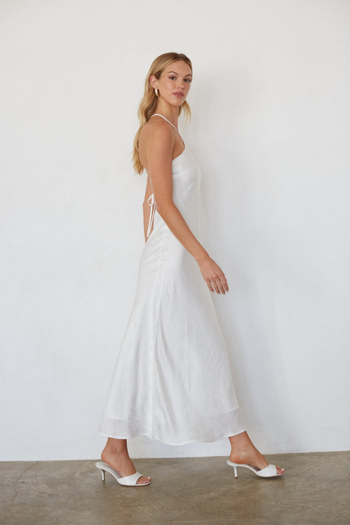 Woman wearing a white dress with cut-out sides against a plain background