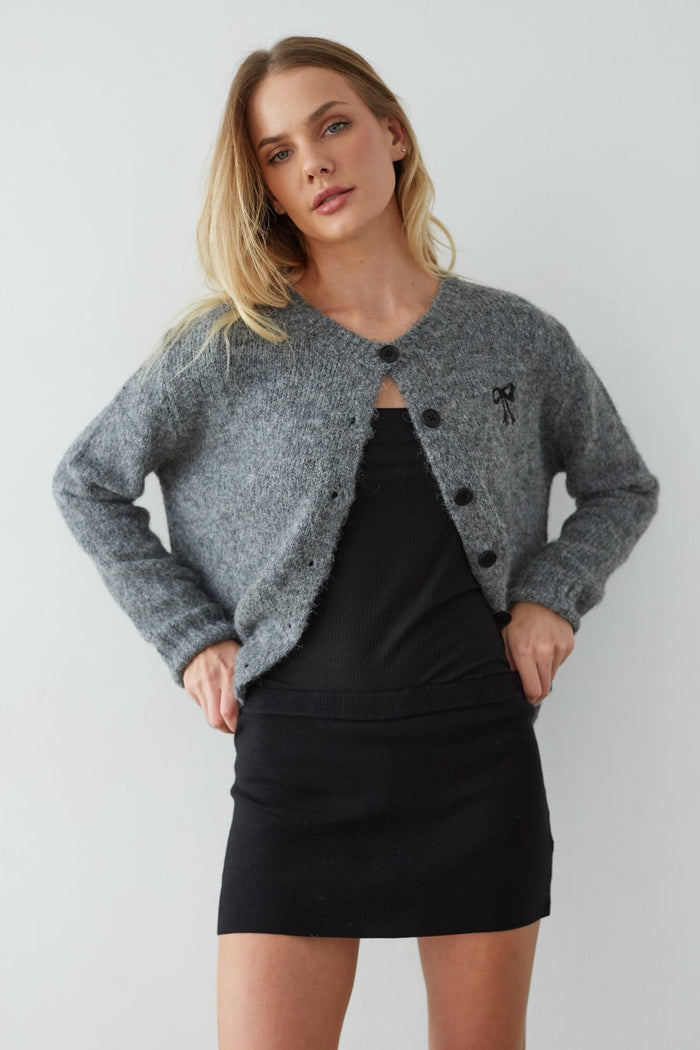 Woman wearing a gray cardigan over a black top and skirt on a white background
