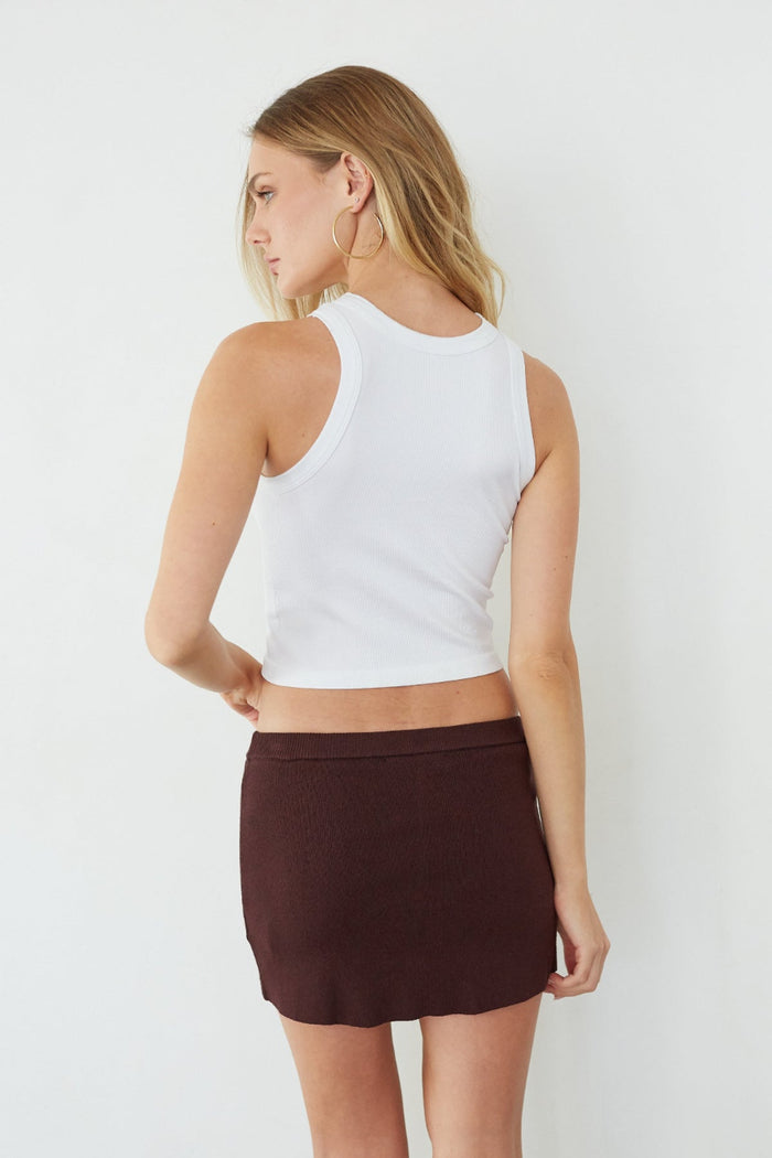 Woman wearing a white tank top and brown skirt on a plain background