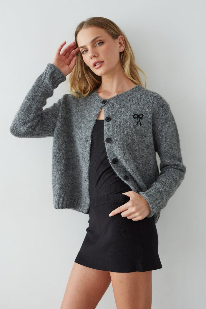 Woman wearing a gray cardigan with a black bow detail on a white background