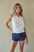 Woman wearing a white sleeveless top and blue shorts against a plain background