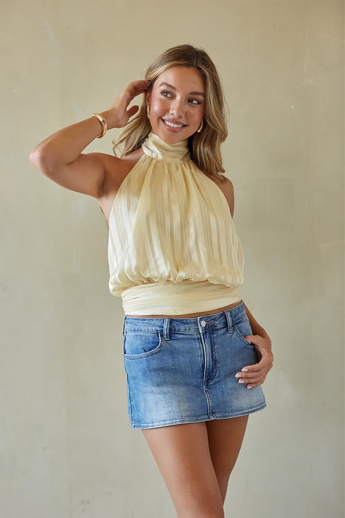 Woman wearing a beige top and denim skirt against a plain background