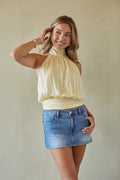 Woman wearing a beige top and denim skirt against a plain background