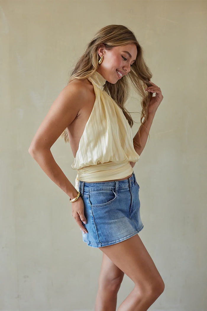 Woman wearing a yellow halter top and denim skirt against a plain background