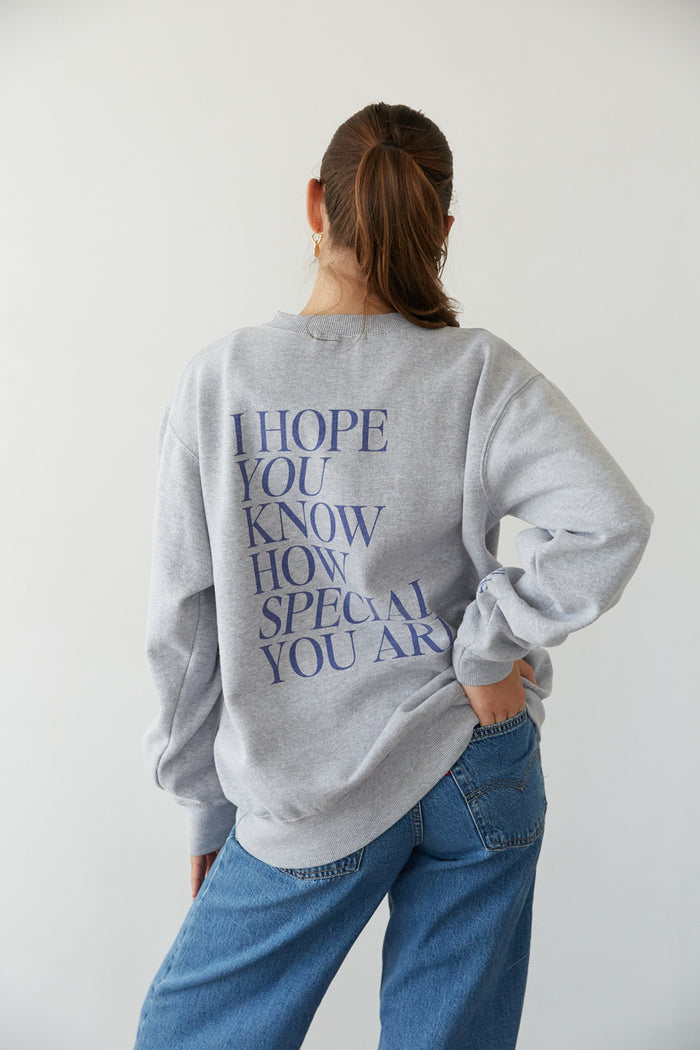 A person wearing a gray crewneck sweatshirt with text on the back standing against a white background.