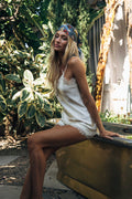 Woman in a white lace dress sitting outdoors with greenery in the background