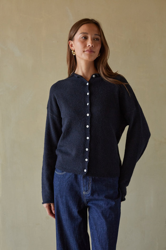 Woman wearing a dark blue cardigan with white buttons against a beige background