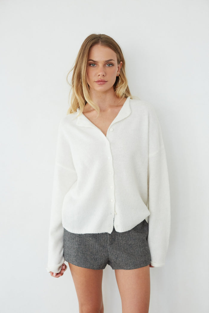 Woman wearing a white blouse and gray shorts against a white background