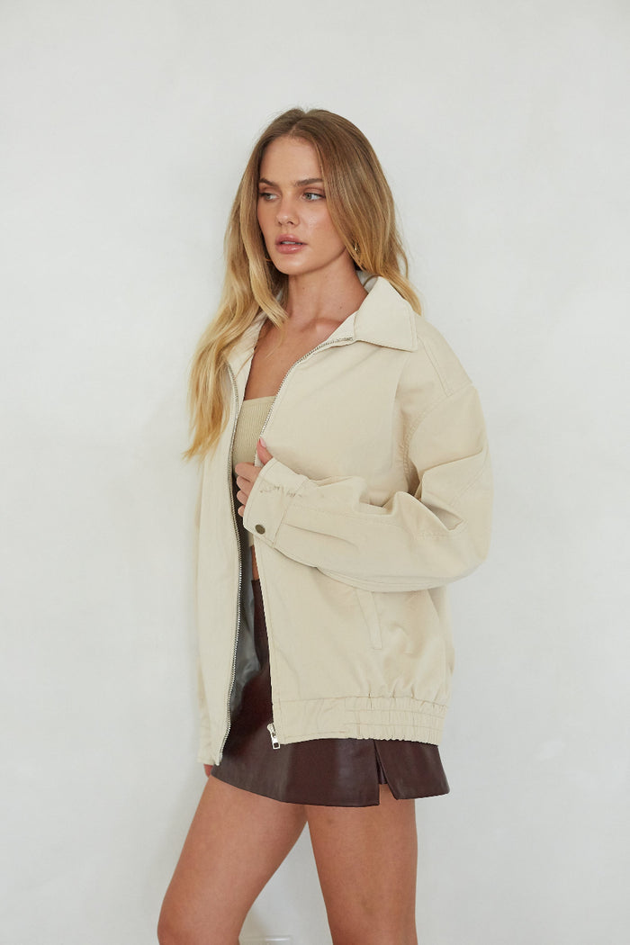 Woman wearing a beige jacket over a black top and brown shorts on a white background