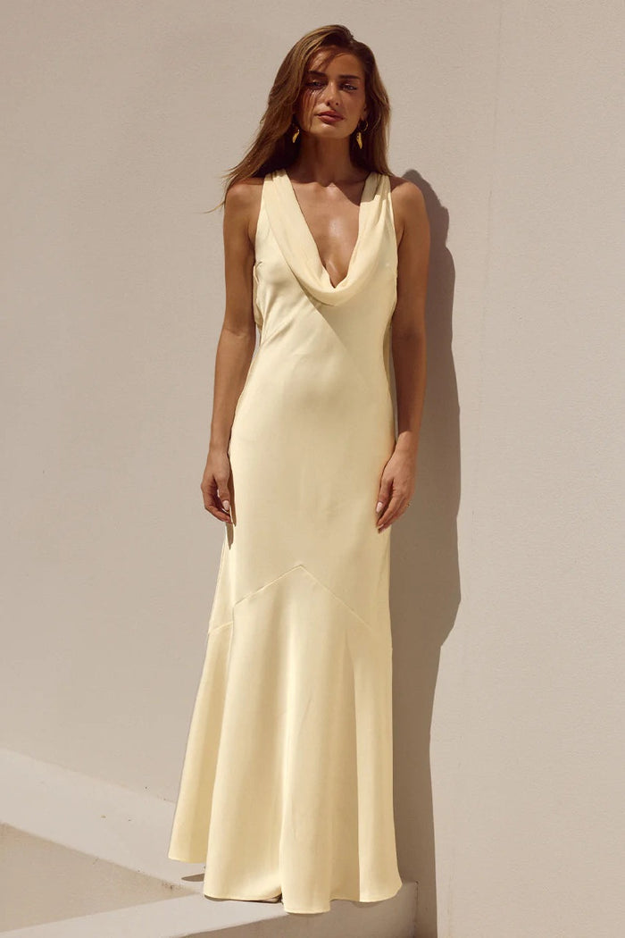 yellow-image | Woman wearing a beige sleeveless dress against a neutral background