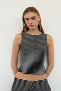 A woman modeling a sleeveless black and white horizontally striped crop top with a button-down front, paired with matching striped bottoms, against a plain white background.