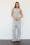 A woman modeling a matching two-piece loungewear set consisting of a sleeveless cropped top and wide-leg pants, both in a gray and white striped pattern, standing against a plain white wall.
