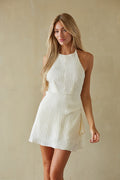 Woman wearing a white halter neck dress against a beige background