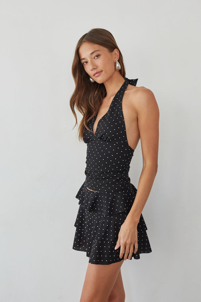 Side-image | Polka Dot Mini Skort | side view featuring a black halter neck top with white polka dots, paired with a tiered, ruffled skirt.