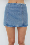 A light blue denim mini skirt worn by a model, shown from the waist down against a plain light gray background.
