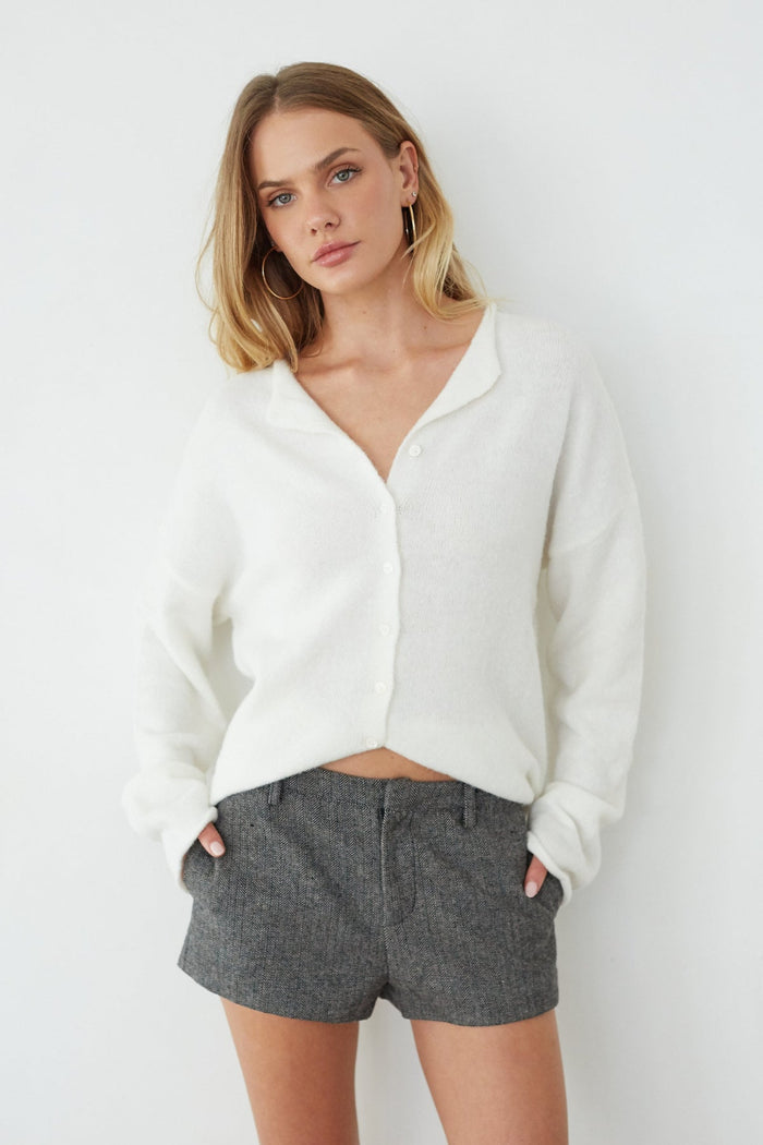 Woman wearing a white cardigan and gray shorts against a white background