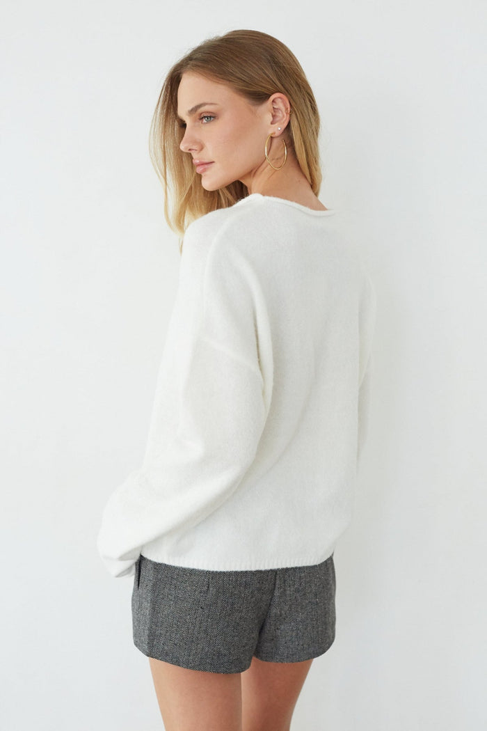 Woman wearing a white sweater and gray shorts on a plain background