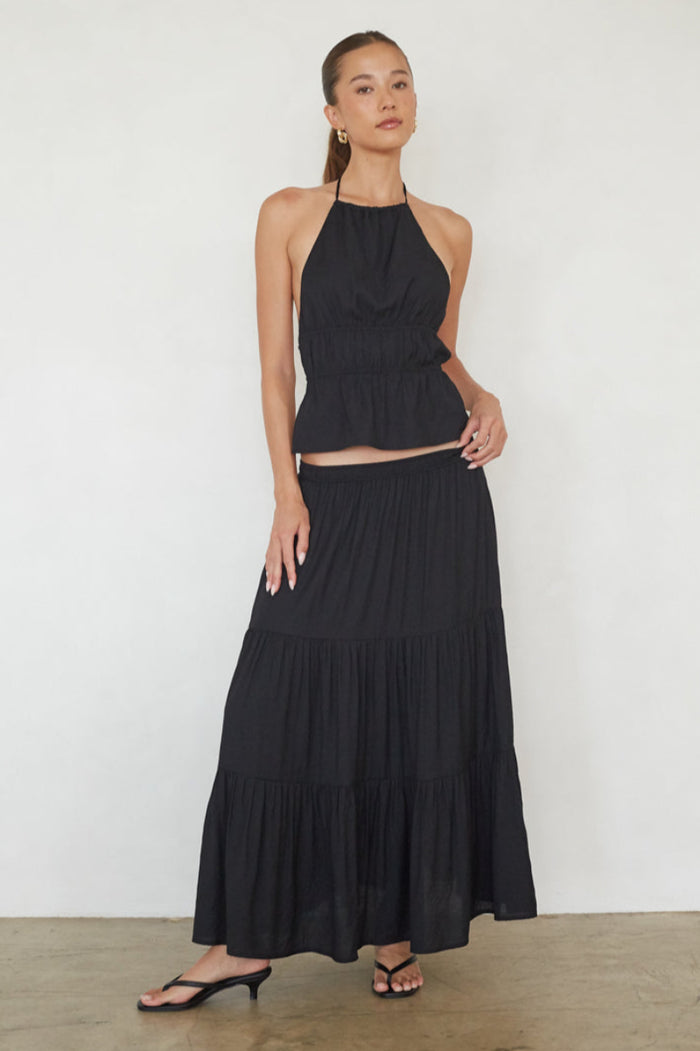 Woman wearing a black halter neck dress standing against a white wall.