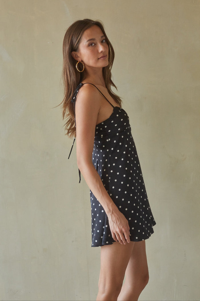 Woman wearing a black dress with white polka dots against a beige background
