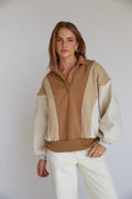 A female model wearing a beige and brown color block pullover sweatshirt with a button-up neckline.