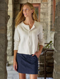 A woman wearing a cream-colored long-sleeve button-up shirt and a navy blue mini skirt, standing in a stone corridor.