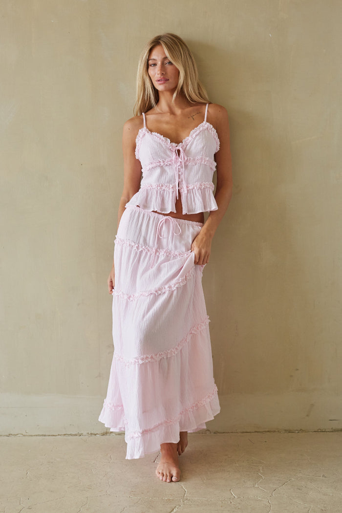 Woman wearing a pink lace outfit against a beige wall.
