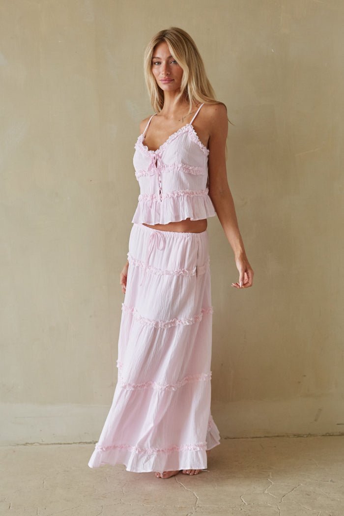 Woman wearing a pink ruffled top and skirt set against a beige wall.