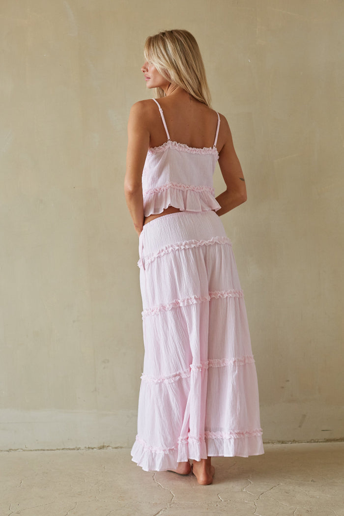 Woman wearing a pink ruffled dress against a beige wall.