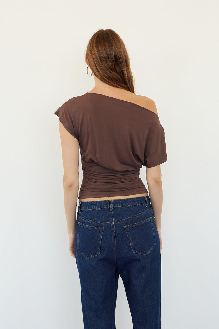 A woman shown from the back wearing a brown off-the-shoulder crop top and dark blue jeans against a plain white background.