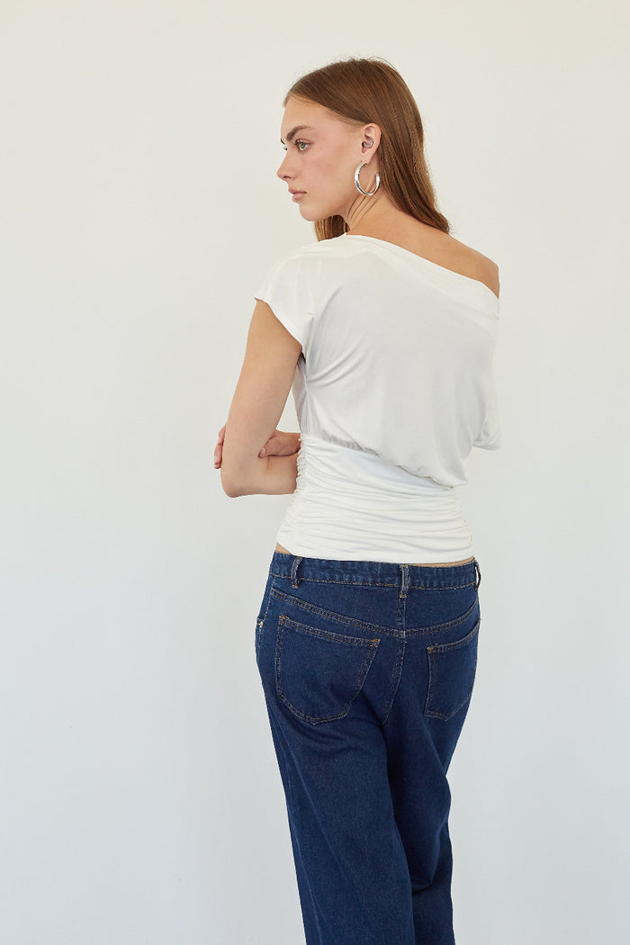 A woman shown from the back wearing a white off-the-shoulder short-sleeve top and dark blue jeans against a plain light gray background.