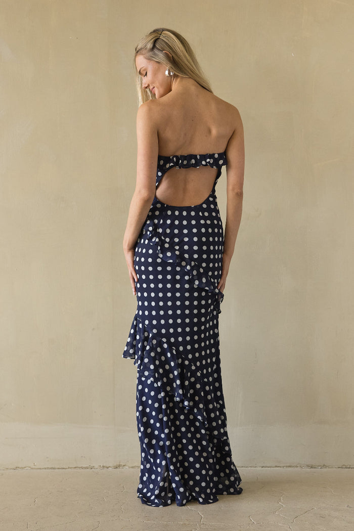 Woman wearing a navy blue strapless dress with white polka dots against a beige wall.