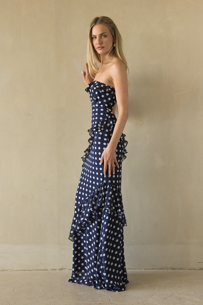 Woman wearing a strapless navy blue dress with white polka dots against a beige wall.