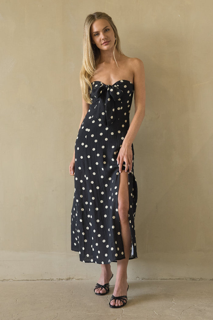 black-image | Woman wearing a black strapless dress with white polka dots against a beige wall.