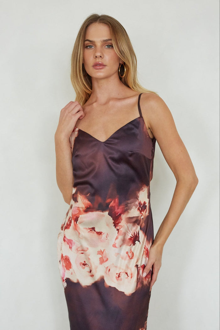 Woman wearing a floral satin slip dress against a plain background