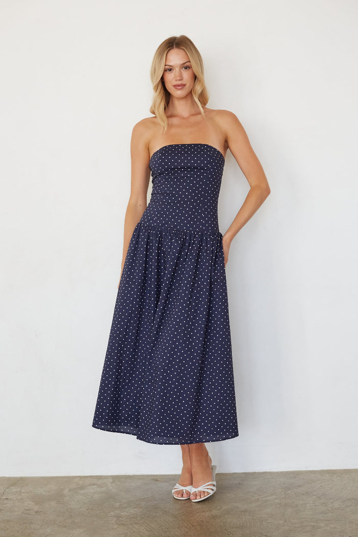 blue-image | Woman wearing a strapless navy polka dot dress against a white background