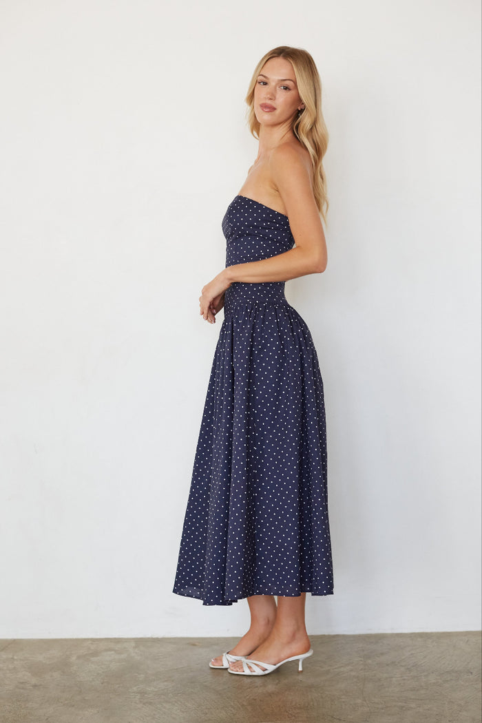 Woman wearing a strapless navy dress with white polka dots against a plain background