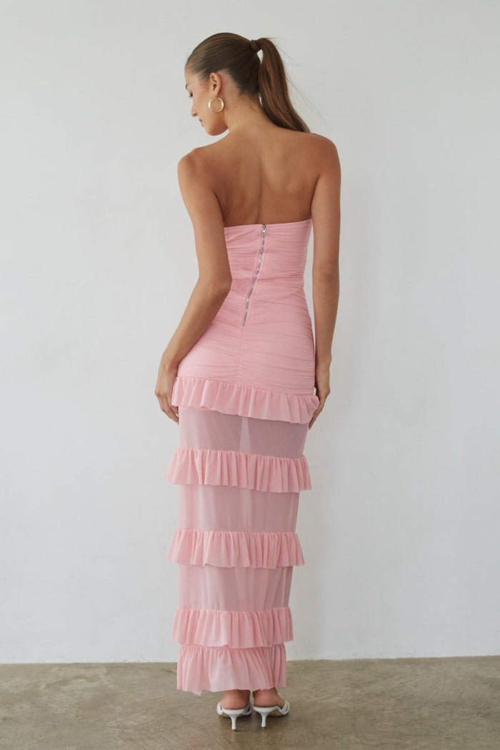 Woman wearing a pink strapless dress with ruffled layers on a plain background