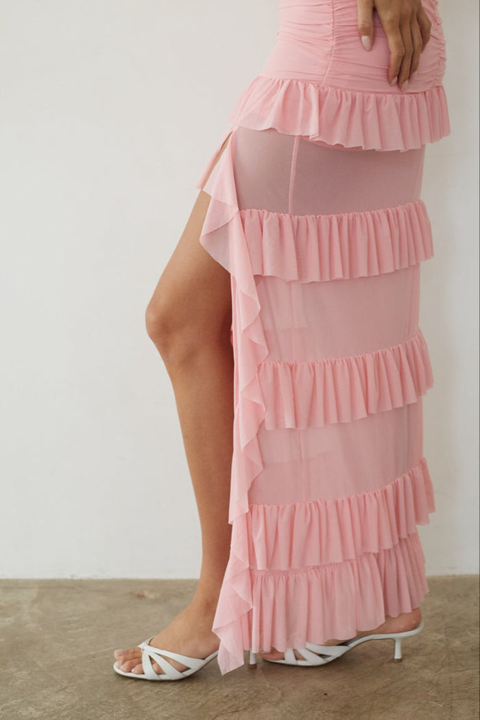 Pink ruffled dress with a high slit on a plain background
