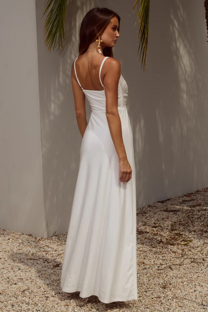 Woman in a white dress standing against a neutral wall with palm leaves.