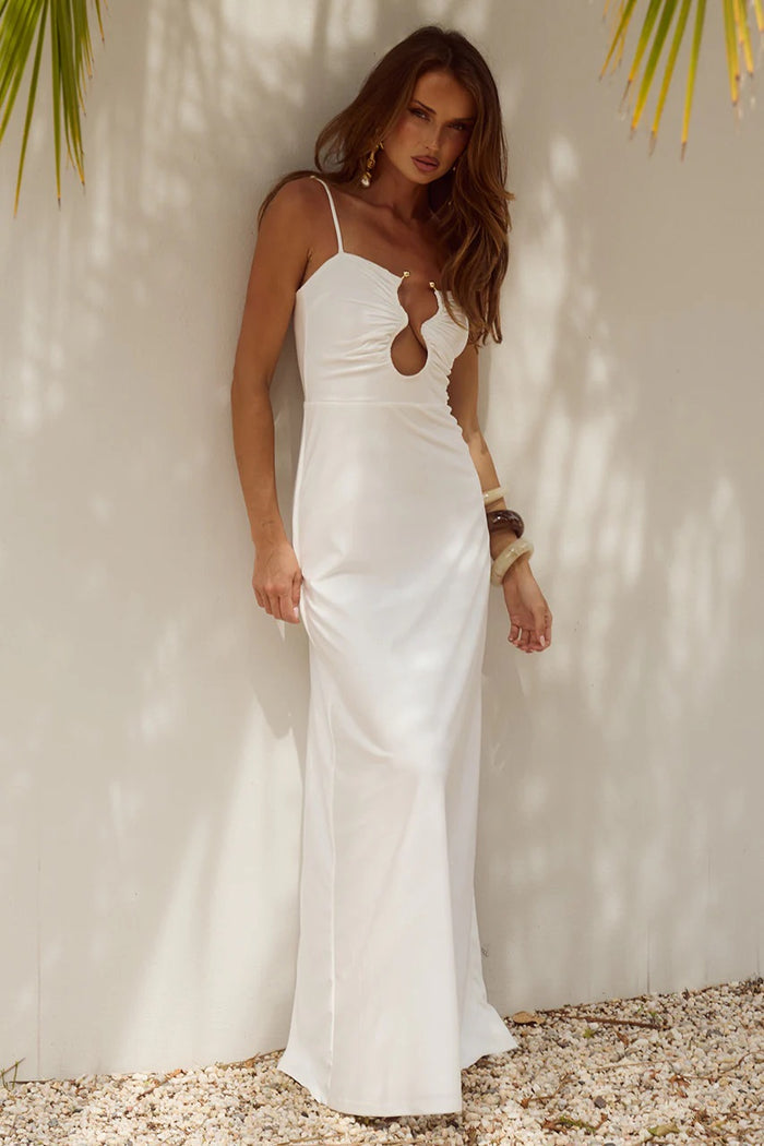 Woman in a white dress standing against a light background with palm leaves.