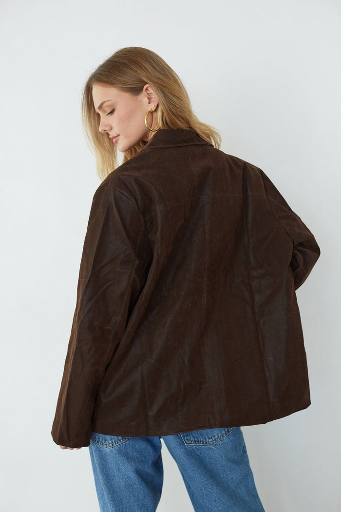 Person wearing a brown jacket and blue jeans against a white background