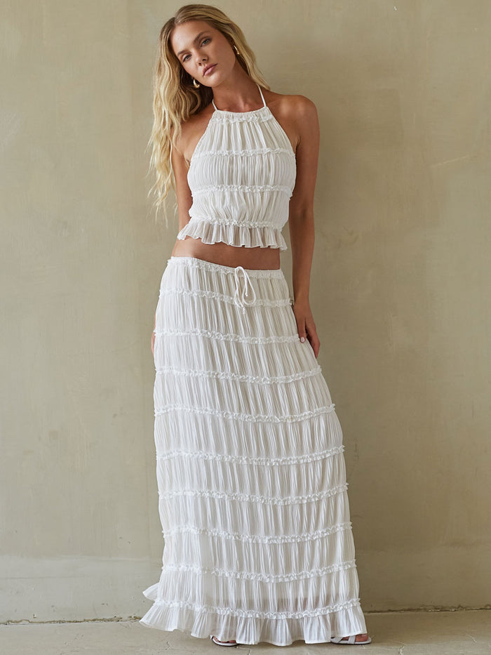 Woman wearing a white ruffled top and skirt against a beige background