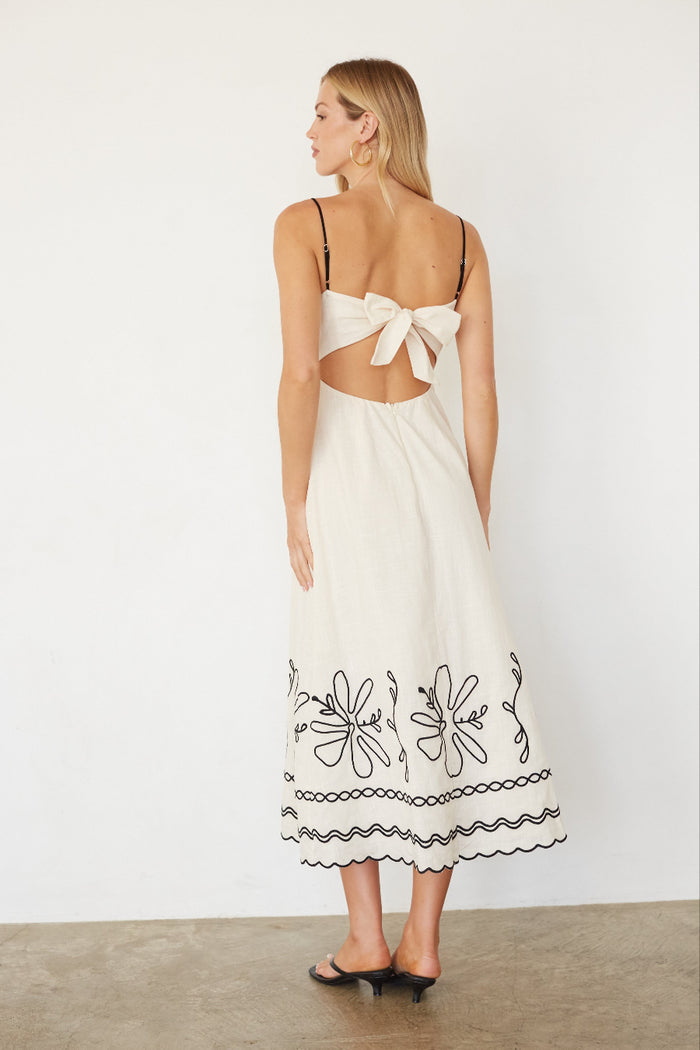 Woman wearing a white dress with floral embroidery on a plain background