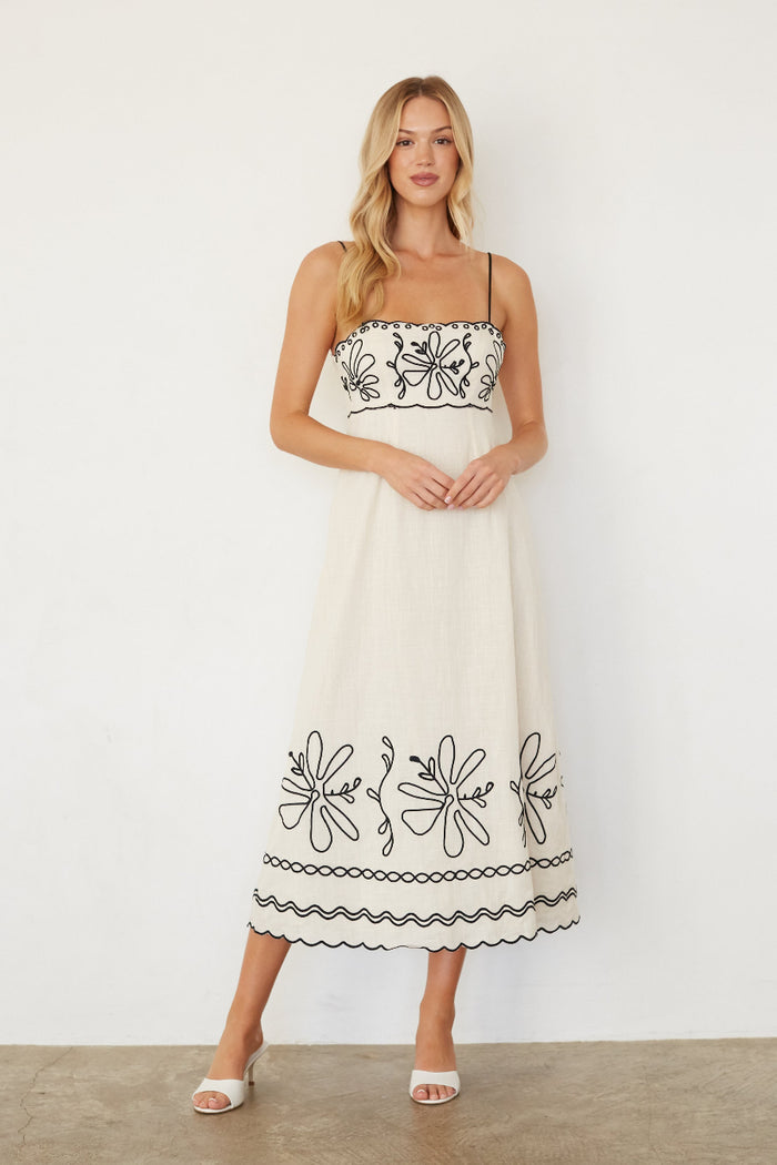 Woman wearing a white dress with black embroidery against a white background