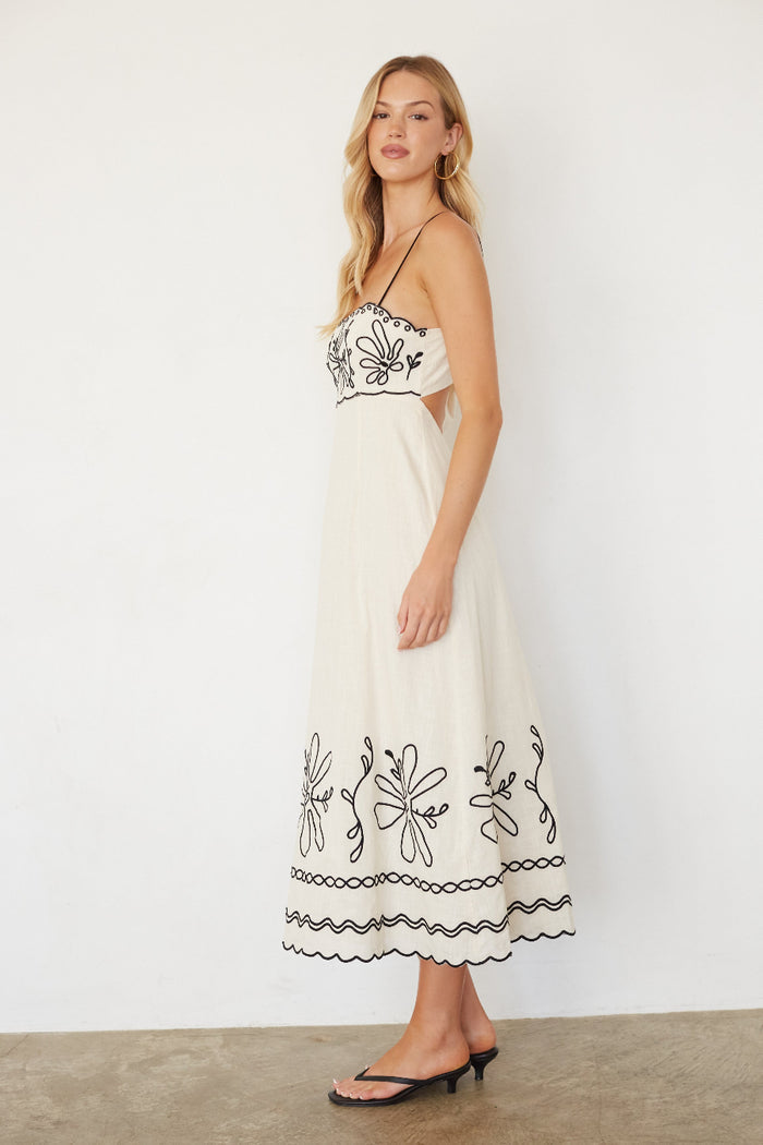 Woman wearing a white dress with black embroidery against a plain background