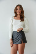 front view: black side slit faux leather mini skort styles with a square neck puff sleeve sweater in white