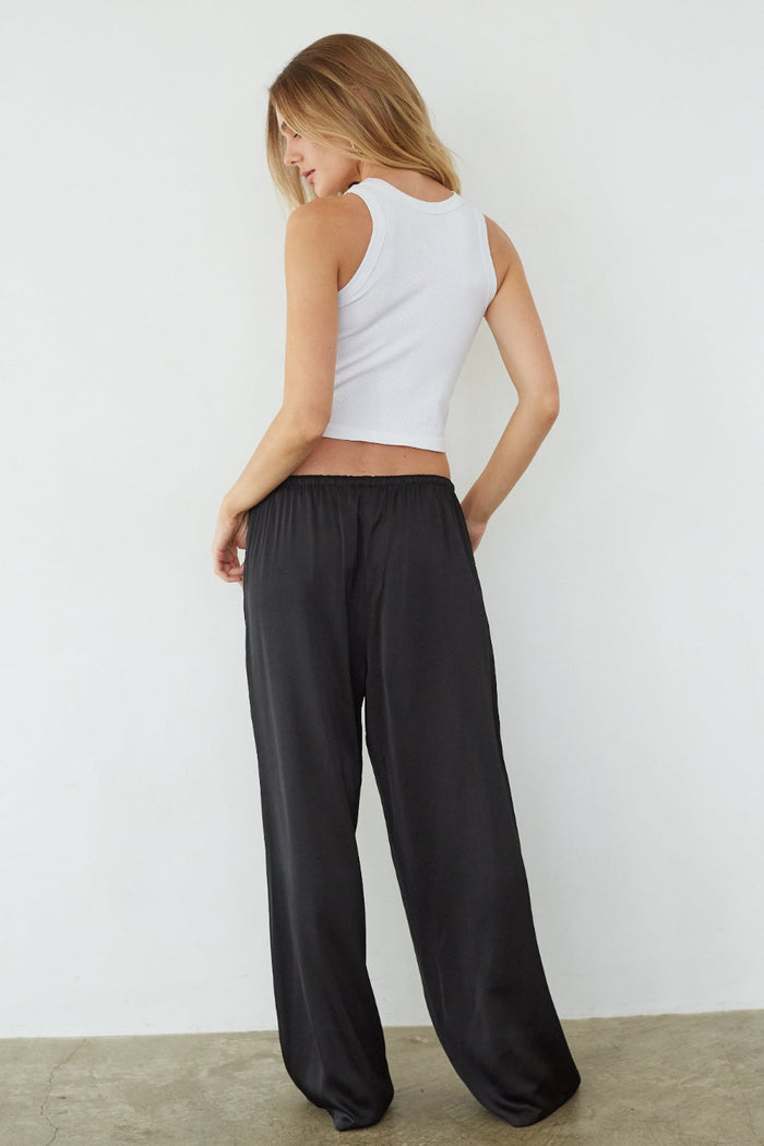 Woman wearing a white tank top and black wide-leg pants against a plain background